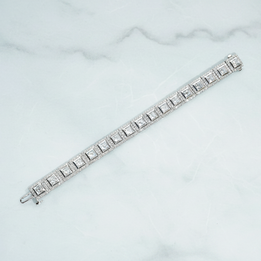 Silver bracelet on a white surface with green foliage