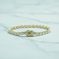 Gold bracelet with clear stones on a light surface with green foliage in the background