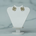 Pair of gold earrings on a white jewelry stand with a plant in the background