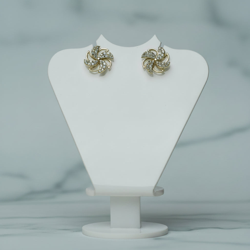 Pair of gold earrings on a white jewelry stand with a plant in the background