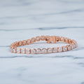 Rose gold bracelet with diamonds on a beige surface with green leaves in the background