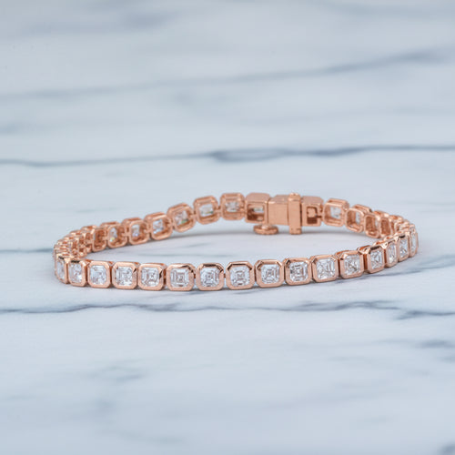 Rose gold bracelet with diamonds on a beige surface with green leaves in the background