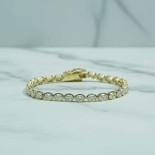 Gold bracelet with clear stones on a light surface with green foliage in the background