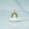 Gold rainbow-shaped pendant on a white background with greenery and flowers.