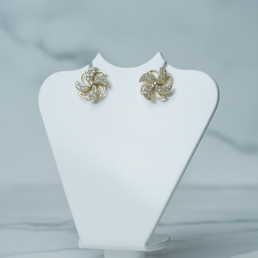 Gold earrings on a white mannequin bust with a blurred green plant in the background